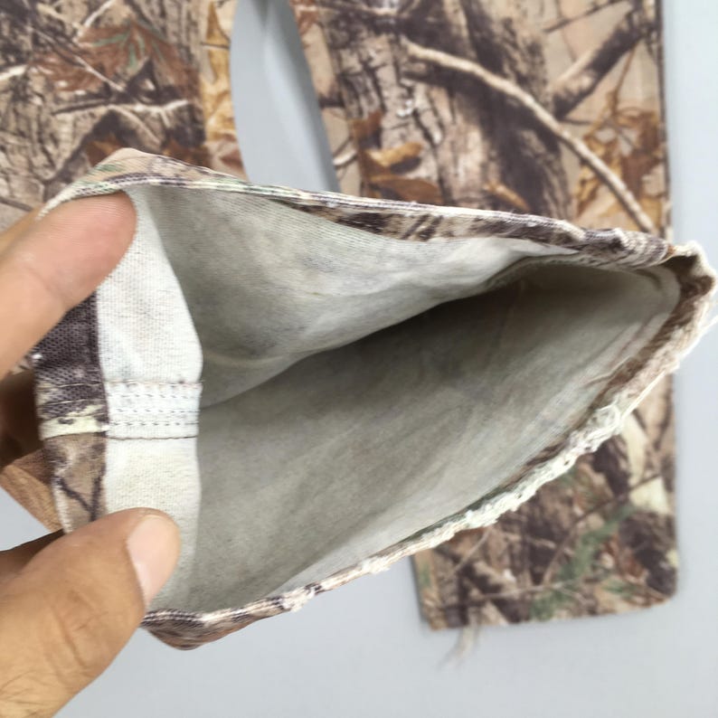 K&ouml;nnte beinhalten: Nahaufnahme eines Camouflage-Hosenbeins, das das Innenfutter zeigt. Die Hose hat ein realistisches Baumrindenmuster in Braun-, Beige- und Gr&uuml;nt&ouml;nen. Das Innenfutter ist ein hellgrauer Stoff. Der Saum ist umgeschlagen und zeigt die Innennaht.