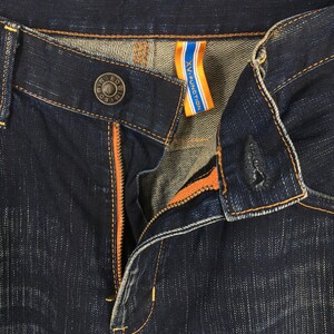 May include: Close-up of dark blue denim jeans with orange stitching and a visible zipper. The jeans have a button closure with the text "WIN ED BD" and a tag that reads "XV-FUNCTION" in white and blue.