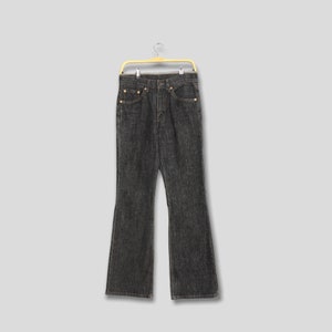 May include: Dark gray denim jeans with a flared leg design, hanging on a yellow hanger. The jeans have classic five-pocket styling with brass rivets and a button closure. The fabric appears to be a medium weight.
