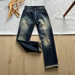 Könnte beinhalten: Dunkelblaue Jeans aus Indigo-Denim mit kontrastreicher Waschung an Oberschenkeln und Knien, Knopfleiste und sichtbaren Webkanten an den umgeschlagenen Säumen. Der Denim-Stoff zeigt eine strukturierte Passform mit verstärkten Nähten an den Seiten.