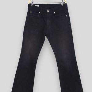 May include: Dark wash denim jeans with a subtle flare at the hem, suspended on a gold-coloured hanger. The jeans feature a classic five-pocket design with a button and zip closure. The fabric appears to be a medium-weight denim.