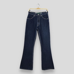 May include: Dark wash denim jeans with a flared leg. The jeans are hanging on a gold-colored hanger. The jeans have a button and zipper closure, with pockets on the front and back. The jeans are a classic style.