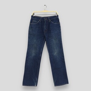 May include: Dark blue denim jeans hanging on a gold-colored hanger. The jeans have a classic five-pocket design with a button and zipper closure. The denim has a slightly faded appearance, with subtle wear marks.