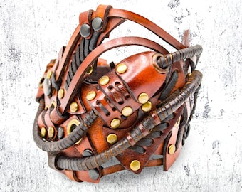 May include: A brown leather bracelet with intricate details, featuring a steampunk design with metal accents and braided leather straps.