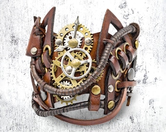 May include: Brown leather steampunk cuff bracelet with brass and silver gears, rivets, and metal tubing accents. The wide cuff features a unique design with cut-out shapes and intricate detailing, creating a bold, industrial aesthetic.