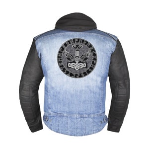 Könnte beinhalten: Eine blaue Jeansjacke mit schwarzen Lederärmeln. Die Rückseite der Jacke zeigt ein weiß gesticktes Design eines Hammers und Runen in einem Kreis.