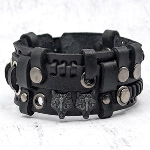 May include: Black leather bracelet with silver metal accents and wolf head designs. The bracelet is adjustable and has a braided leather strap.