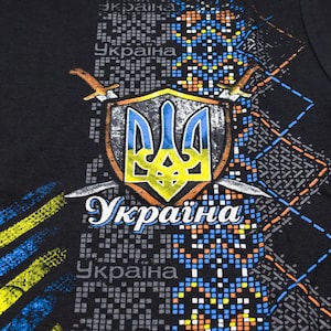 May include: Black t-shirt with a blue and yellow Ukrainian coat of arms, two swords, and the word "Україна" (Ukraine) printed on it.