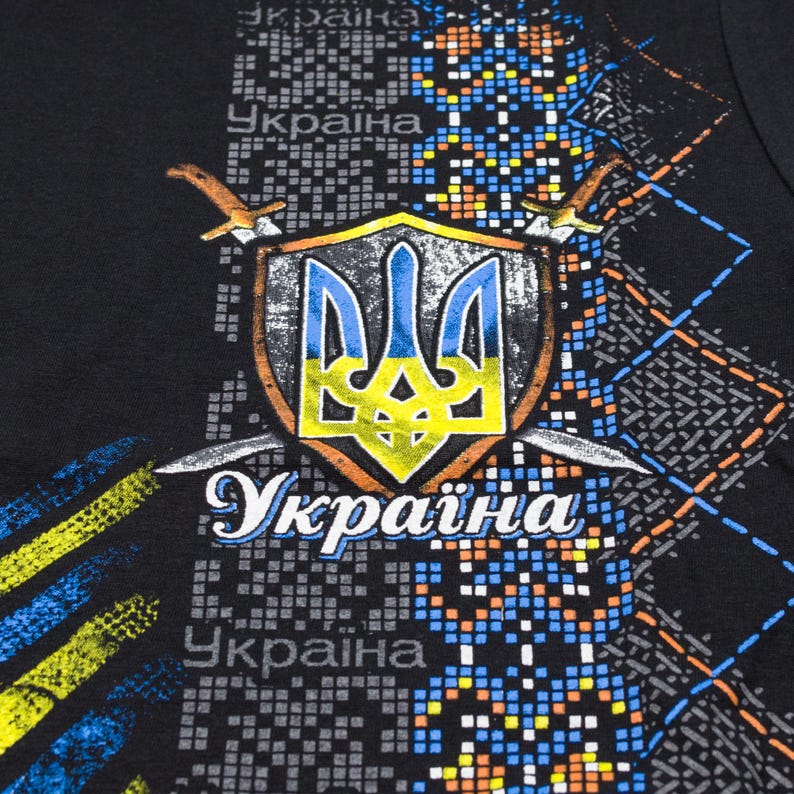May include: Black t-shirt with a blue and yellow Ukrainian coat of arms, two swords, and the word "Україна" (Ukraine) printed on it.