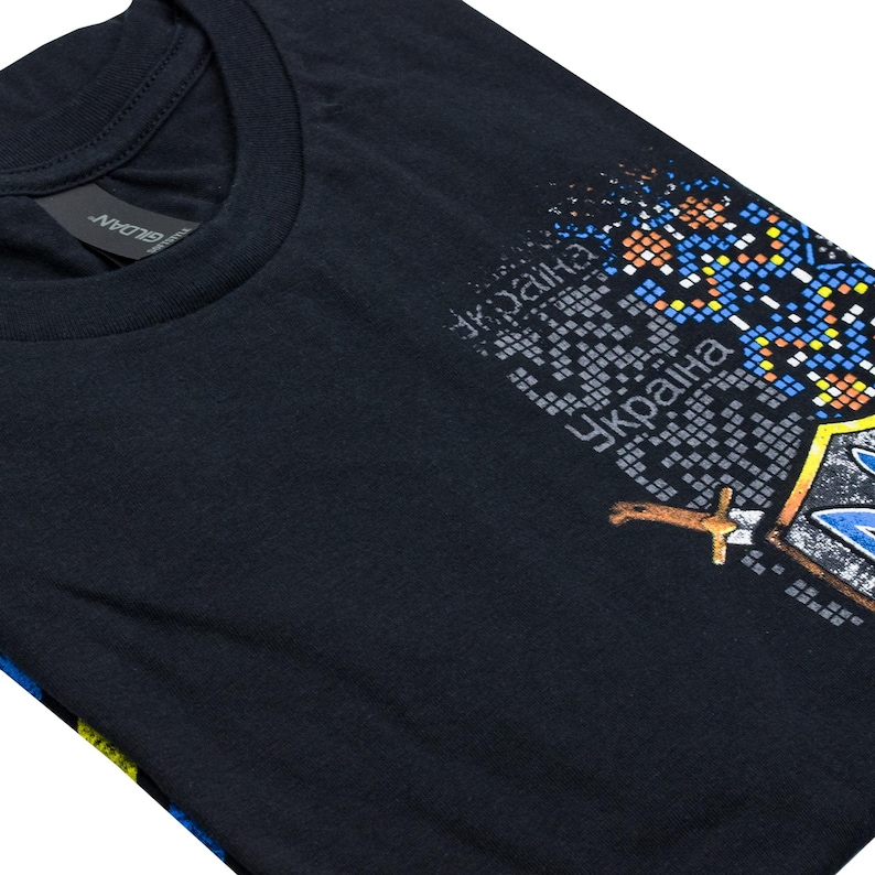 May include: A black t-shirt with a graphic print of a stylized Ukrainian coat of arms. The graphic is made up of pixelated squares in blue, yellow, red, and white. The text "Україна" is printed in black on the graphic.