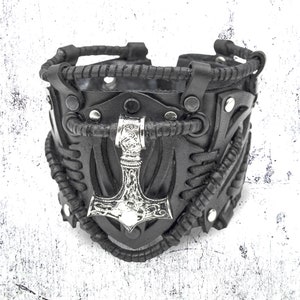May include: Black leather bracelet with a silver-toned metal hammer charm. The bracelet has a braided leather design and metal studs.