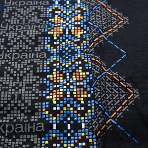 May include: Black fabric with a pixelated design featuring the word "україна" repeated multiple times. The design includes blue, orange, yellow, and white squares.