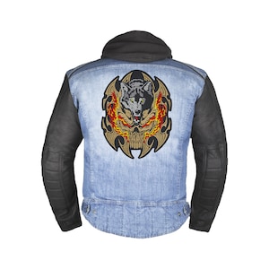 Puede incluir: Una chaqueta vaquera azul con mangas de cuero negro presenta un gran parche bordado en la espalda. El parche representa una cabeza de lobo con llamas y una calavera en un diseño tribal.