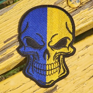 May include: A blue and yellow skull patch with an embroidered design. The skull is split down the middle, with one side blue and the other yellow.