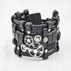 May include: Black leather bracelet with silver gears and rivets. The bracelet is wide and has a steampunk aesthetic.