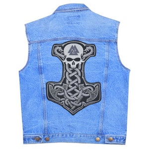 May include: A light blue denim vest featuring a large, detailed patch. The patch depicts a stylized hammer with a skull, intricate knotwork, and a triangular symbol. The design is primarily gray and black.