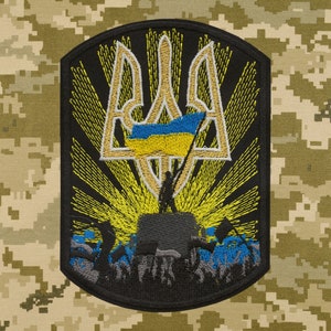 May include: Embroidered patch depicting the Ukrainian coat of arms, a golden trident, with a blue and yellow flag. The trident is surrounded by a yellow sunburst and a crowd of people raising their hands in the air.