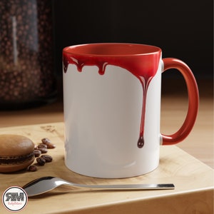 May include: White ceramic mug with a red rim and red dripping paint design. The mug has a handle.