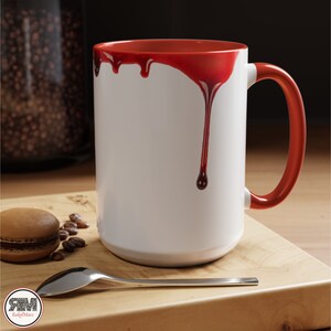 May include: White ceramic mug with a red rim and red dripping paint on the side. The mug has a handle.