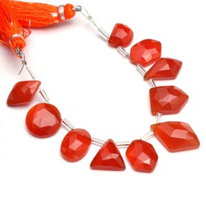 May include: A strand of carnelian gemstone beads, featuring faceted, orange-red stones of various shapes, including round, oval, and triangular. The beads are strung on silver wire and finished with a tassel.