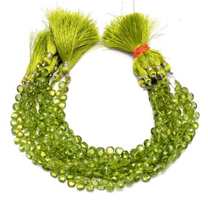 May include: A collection of faceted, heart-shaped lime green peridot beads strung on multiple strands. Each strand is finished with a vibrant lime green silk tassel featuring silver-toned metal caps, with one tassel secured by a bright orange rubber band.