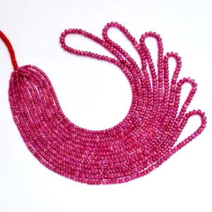 Könnte beinhalten: Stränge aus kleinen, runden, tiefrosa Perlen vor weißem Hintergrund. Die Perlen sind aufgefädelt, mit einem roten Faden oben links, wahrscheinlich für die Schmuckherstellung.