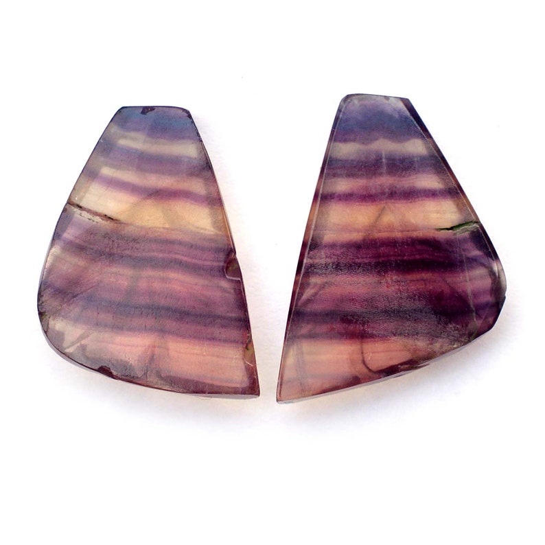 K&ouml;nnte beinhalten: Zwei violette, rosa und wei&szlig;e gestreifte Fluorit-Cabochons. Die Cabochons sind in einer dreieckigen Form mit abgerundeten Kanten geschnitten.