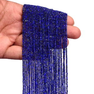 Peut inclure: Plusieurs brins de petites perles bleues foncées et facettées. Les perles sont enfilées ensemble, créant un aspect dense. Les perles sont tenues dans une main, mettant en valeur leur couleur. Idéal pour la création de bijoux.