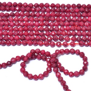 Può includere: Un filo di perle di corallo rosso, con una texture ruvida e sfaccettata. Le perle sono infilate su un filo rosso e hanno un diametro di circa 6 mm.