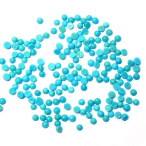 Op de afbeelding: Een verzameling kleine, ronde turkoois edelstenen verspreid op een witte ondergrond. De edelstenen variëren in tint, van licht- tot middeldiep blauw. De gladde, gepolijste stenen zijn ideaal voor sieraden maken of knutselprojecten.