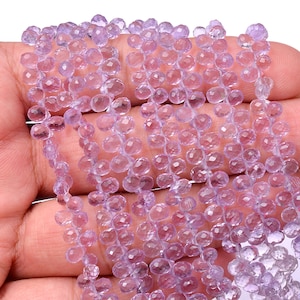 Peut inclure: Gros plan sur des brins de perles de pierres précieuses violet clair. Les perles sont facettées et en forme de goutte d'eau, enfilées ensemble pour créer un effet délicat et chatoyant. Les perles sont tenues dans une main, mettant en valeur leur couleur et leur texture.