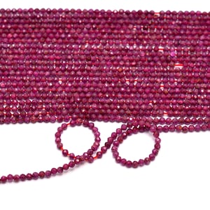 Może przedstawiać: Szereg fasetowanych koralików z rubinowego kamienia szlachetnego. Koraliki są małe i okrągłe, a nawleczone są na cienki sznurek. Są też dwa mniejsze sznury koralików, które ułożone są w kształt koła.