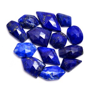May include: A collection of twelve faceted lapis lazuli gemstones in various shapes and sizes. The stones are a deep blue colour with flecks of gold pyrite.