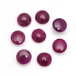 May include: Eight polished, circular gemstones in shades of deep red and purple are displayed against a white backdrop. The gemstones are arranged in a circular pattern. Each stone has a smooth, reflective surface.