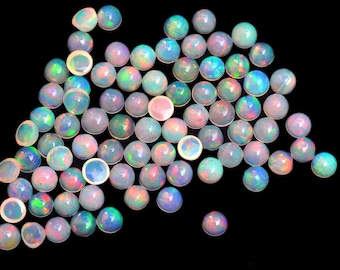May include: A collection of round, iridescent opal cabochons in various shades of white, blue, green, and pink. The opals are scattered on a black background.