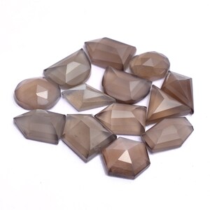 May include: A collection of twelve grey gemstone cabochons in various shapes, including round, oval, and rectangular. The stones are faceted and have a smooth, polished finish.
