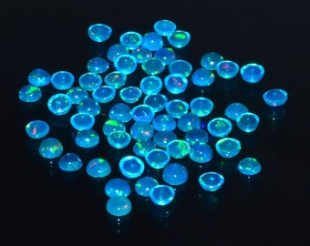 May include: A collection of blue opal cabochons, with iridescent green and pink flashes, scattered on a black background.