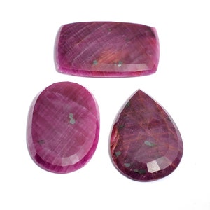 Puede incluir: Tres piedras preciosas de rubí rosa con un corte facetado. Las piedras preciosas son de diferentes formas: un rectángulo, un óvalo y una lágrima.