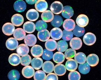 May include: A collection of iridescent opal cabochons in various shades of blue, green, and white. The cabochons are round and have a smooth, polished surface.