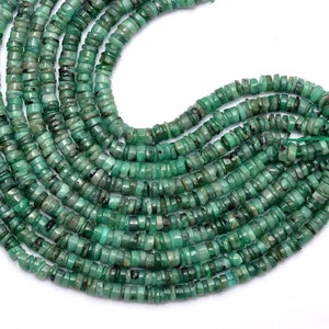 以下が含まれることがあります： エメラルドグリーンの宝石ビーズのストランド。各ビーズは、丸みを帯びたエッジを持つ平らな長方形の形をしています。ビーズは細い糸に糸に通され、緩やかな流れのあるパターンで配置されています。