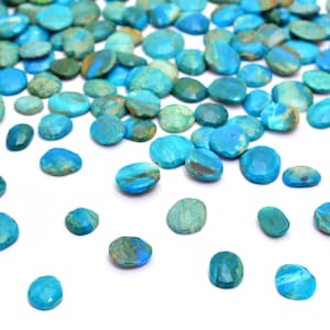 Op de afbeelding: Een verzameling turquoise blauwe edelsteen cabochons, verspreid over een witte achtergrond. De cabochons zijn ovaalvormig en hebben een gevlekt patroon.