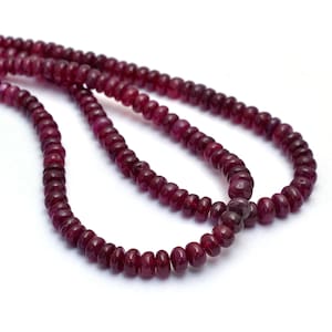 May include: A strand of deep red ruby beads, strung together to form a necklace. The beads are round and smooth, with a slight sheen.