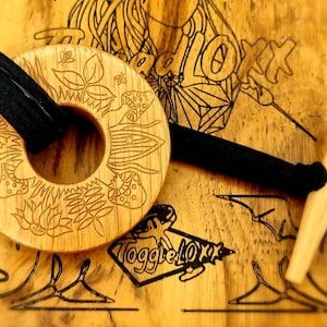 May include: A wooden toggle with a floral design and a black strap. The toggle is engraved with the words "Toggle Love" and "Redlox".