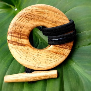 May include: A wooden music note hair tie with a black elastic band. The hair tie is round and has a hole in the center. The music notes are carved into the wood.