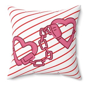 May include: Square throw pillow with a white background and red diagonal stripes. The pillow features a pink heart-shaped handcuff design connected by a chain. The design is a playful take on love and relationships.