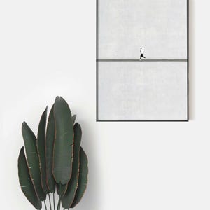 May include: A framed minimalist art print featuring a person running on a gray line against a textured white background. The artwork is encased in a black frame. A large green plant with long leaves is in the foreground.