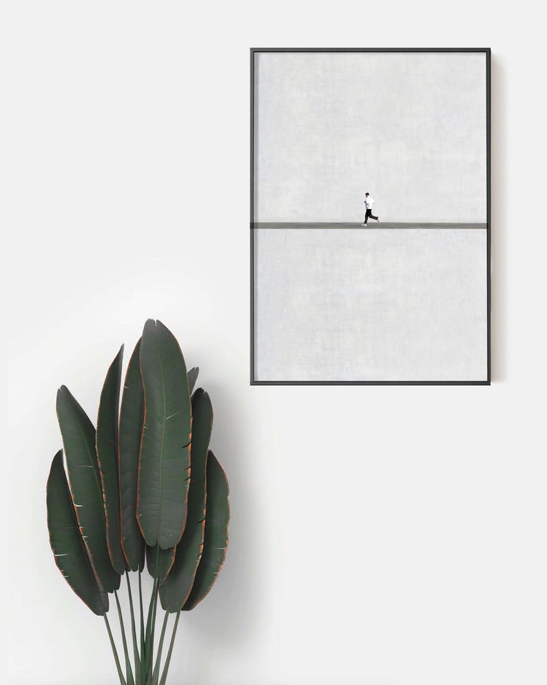 May include: A framed minimalist art print featuring a person running on a gray line against a textured white background. The artwork is encased in a black frame. A large green plant with long leaves is in the foreground.