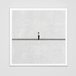May include: A square art print featuring a small figure standing in the center of a vast, empty space. The composition is divided horizontally by a dark line, separating a textured light gray upper section from a matching lower section.