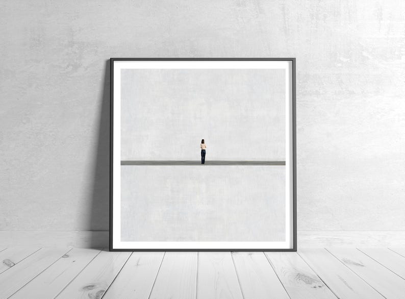 May include: A square framed wall art print featuring a minimalist composition with a small figure standing in the center of a horizontal line, set against a vast, light gray background that creates a sense of expansive, open space.