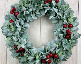 May include: A green and gray wreath with red berries. The wreath is made of faux greenery and is perfect for a holiday or winter decor.